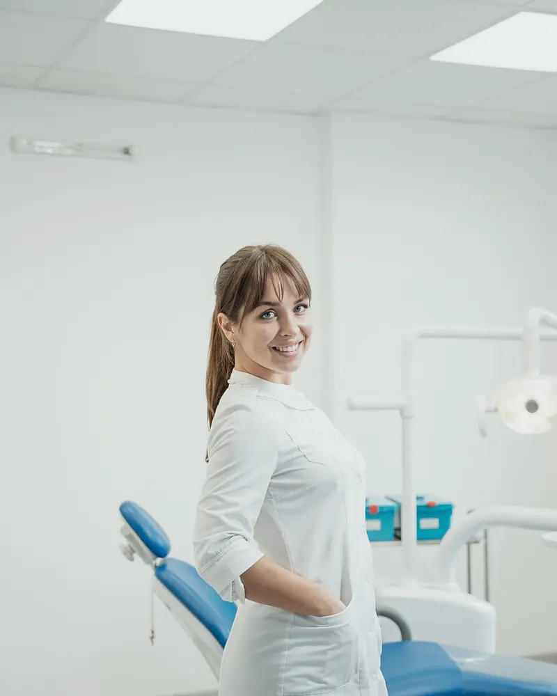 Dentista sorrindo de jaleco branco em consultório odontológico